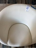 Top view of the white leather cushioned chair seat showing curved backrest and cushion, tagged with lot sticker.