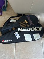 Photo showing black Babolat racket cover and black and gold Spalding Double Play cover with shoulder straps.