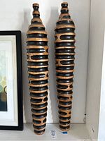 Front view of two tall wooden tower vases showing alternating black recessed stripes and natural wood raised stripes.