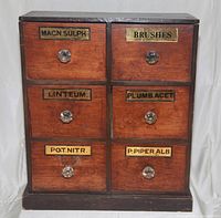Front view showing the six drawers with original brass labels and glass knobs on the dark wooden cabinet.