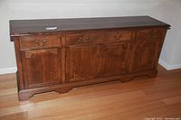 Full front view of the wooden dining room credenza showing its three drawers and three doors with brass handles.