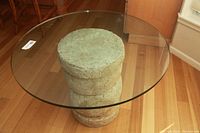 Top view of round glass table with textured concrete-style pedestal base showing glass thickness and scratches.