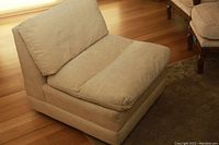 Side and angled view of a beige fabric sofa chair showing cushioned seat and backrest sitting on a wooden floor.