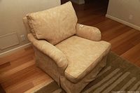 Beige fabric sofa chair with rolled arms, goose down cushion, skirted base, placed on wood floor and rug.