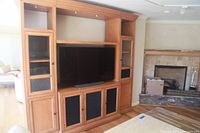 Full front view of the wooden TV wall cabinet with dark mesh doors and a mounted flat-screen TV in the center section.