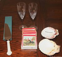 Photo displaying all items laid out on table: 2 champagne flutes, 6 cork coasters with hunt scenes, 8 scallop shells, and 1 cake server with ivory handle.