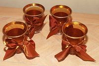 Photo showing four glass votive candle holders with gold interiors and brown satin ribbons tied around each holder.