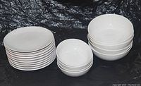 Grouping of 10 white porcelain salad plates stacked, 4 small white stoneware bowls stacked, and 6 large white porcelain bowls stacked.