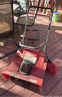 Full view of red Atlas snow blower on wooden deck with accessories nearby.