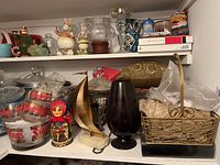 Shelves containing glass bowls with Stanis branding, tiered glass serving tray, Christmas figurines, metal decorative items, and baskets.
