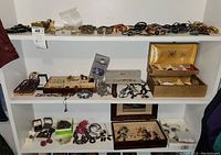 Wide view showing three shelves filled with assorted costume jewelry including bracelets, earrings, necklaces, and jewelry boxes.