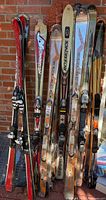 Nine pairs of assorted skis leaning against a brick wall