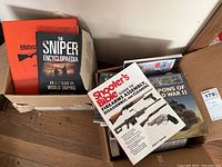 Photo showing box with several firearm and military books including The Sniper Encyclopaedia and Midway shooting sports catalog