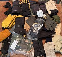 Full lot view showing various pairs of gloves and mitts in multiple colors and materials on a wooden surface.