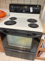 Front view of Kenmore electric oven showing four coil burners, white cooktop and black oven door with window.