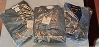 Three navy blue and dark gray outdoor shirts in original plastic packaging, folded with tags visible