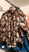 Brown and white patterned men's fleece jacket with zipper and black cuffs hanging on rack