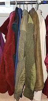 View of eight men’s outerwear items on a clothing rack including fleece, knit, suede, and quilted jackets and sweaters in various colors