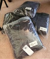 Four men's Polartec shooting jackets sealed in clear plastic packaging with size labels from medium to extra large.