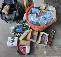 Wide view of tackle bag, reels, spool, and basket of lures on concrete floor