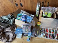 Overall view showing canvas bags, cardboard box with fly fishing line packs, clear tackle box, Ziploc bag of foam baits and attractant jars