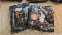 Two folded black and dark plaid outdoor shirts in plastic packaging showing tags and labels with Moose Creek branding.