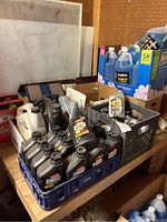 Crate with multiple quart bottles of motor oil and other car fluids on table.
