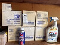 Boxes of Remington Wonder Lube all purpose lubricant aerosol cans and a single spray bottle of Roundup weed killer, unopened on a shelf in a garage.
