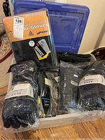 Photo of multiple pairs of black winter gloves in plastic bags and packaging in a blue plastic storage bin.