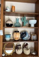 Four shelves filled with various southwestern pottery including vases, cactus decor, bowl, roosters, and mirror