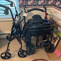 Two rollator walkers and one folding wheelchair grouped together in a room.