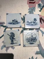 Four antique blue and white ceramic tiles with different traditional Spanish style designs, displayed on a patterned fabric.