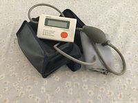 Omron digital blood pressure monitor with cuff and inflation bulb, placed on patterned fabric surface.