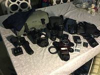 Full view of Canon T70 camera with attached lens, multiple camera bags, lenses, battery chargers, camera flash and other accessories.