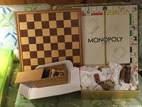 Photo of two boards, chess board and vintage Monopoly board, with two sets of wooden chess pieces, some packed in box and others in tissue
