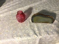 Small cranberry glass jar next to polished agate rock slice on patterned black cloth.
