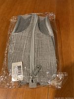 Front view of silver fabric shoe bag with mesh ventilation openings and zipper, sealed in plastic packaging.