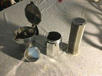 Aluminum Italian coffee maker disassembled in three parts: top chamber with lid open, base chamber, and metal filter funnel.