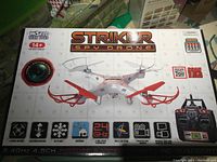 Photo of the Striker Spy Drone unopened in original box, showing front of packaging with product name, images, and feature icons.
