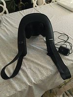 Full view of the black Naipo neck massager with heating function and attached power adapter.