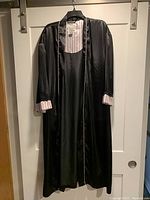 Full view of pink and black satin housecoat hanging on a hanger, visible black outer fabric and pink striped inner lining.