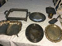 Photo of eight silverplate serving pieces including trays, casserole holder, cup, scoop, and serving dish showing tarnish and use wear.