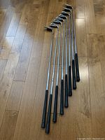 Full set of eight Ping Zing irons including 3-9 and wedge laid out on wooden floor, showing grips and shafts.