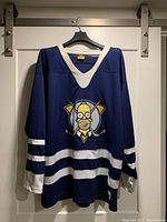 Front view of blue hockey jersey with white stripes and Homer Simpson logo.