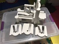 White manual spiralizer with three metal blade inserts laid out in front, set on clear plastic storage container.