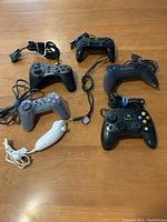Top view of six video game controllers laid on a wooden table showing details of buttons, cords, and connectors