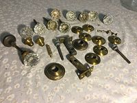 Photo of multiple vintage crystal doorknobs and assorted brass hardware parts laid out on floral patterned cloth.