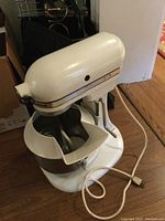 Vintage white Kitchenaid stand mixer assembled with mixing bowl in place on wooden floor.