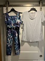 Two-piece tie-dye blue/white crop top and leggings outfit with a light grey short-sleeved coverup shirt, hung on black hangers against a white door.