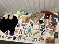 Wide shot of the entire assortment of antique and vintage collectibles including child's jacket, fans, various small containers, books, and more